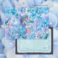 A 5x7 postcard art print featuring a whimsical fairy illustration surrounded by blue and purple hydrangea flowers, shown with the front artwork and a sample back design over a soft blue floral background.